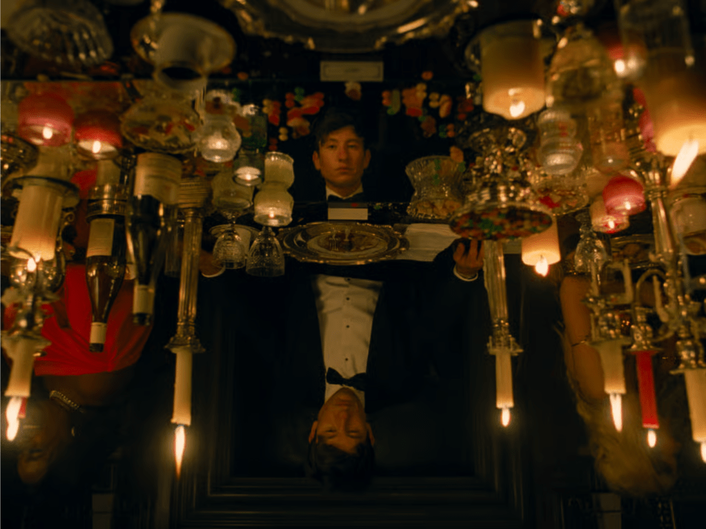 Scene from Saltburn featuring Oliver, played by Barry Keoghan, a white male in black tie surrounded by opulent tableware